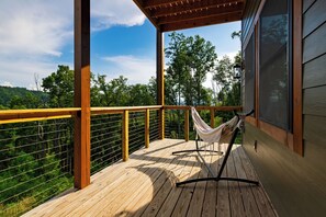 A wooden deck with a hammock, a railing, and a view of a forested area. - Sleeps 40 + 2 Indoor Pools + Game Rooms | The Spurling Collection (Sevierville)