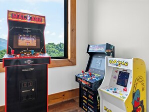 Drei Spielautomaten, einer mit der Aufschrift 'Mortal Kombat', ein anderer 'Pac-Man' und der dritte 'Arcade 2Up'.