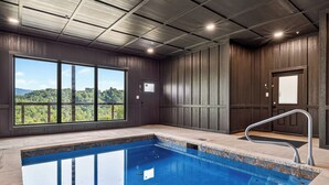 En swimmingpool med utsikt över ett skogslandskap genom stora fönster.