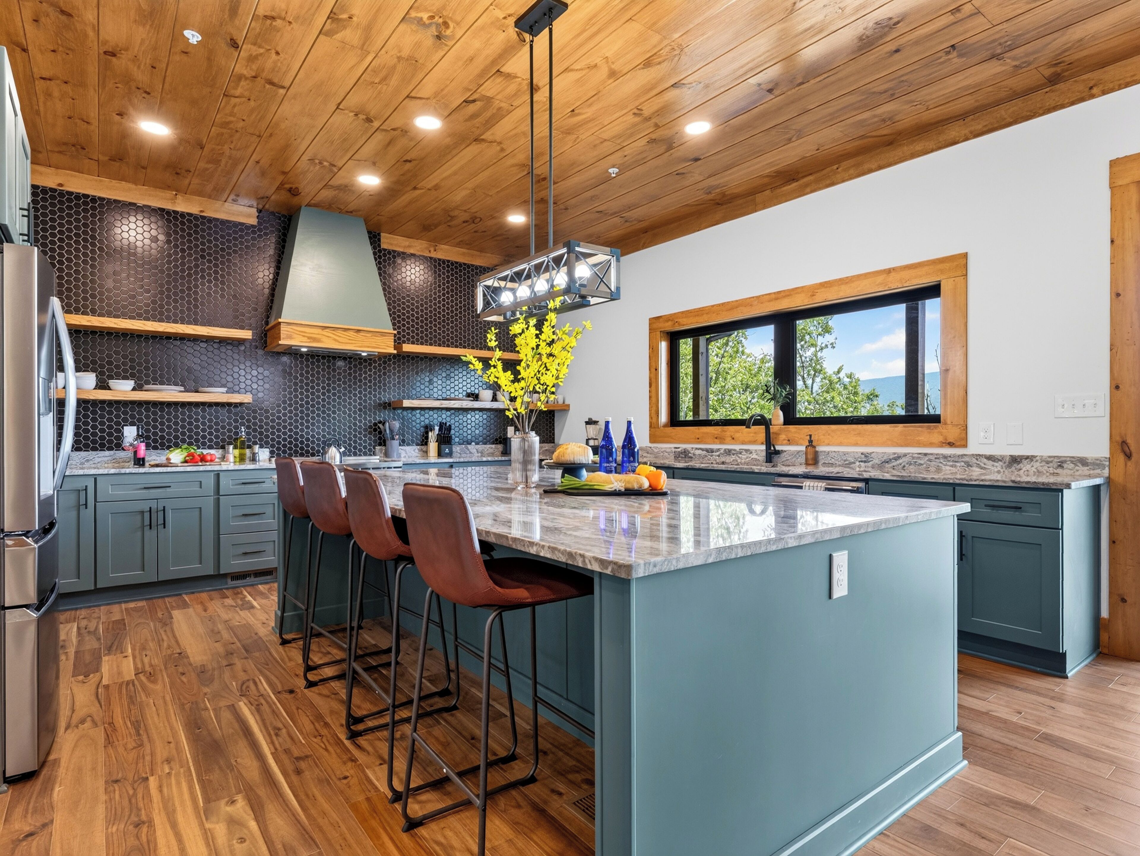 A modern kitchen with a large island, bar stools, and a window with a view.