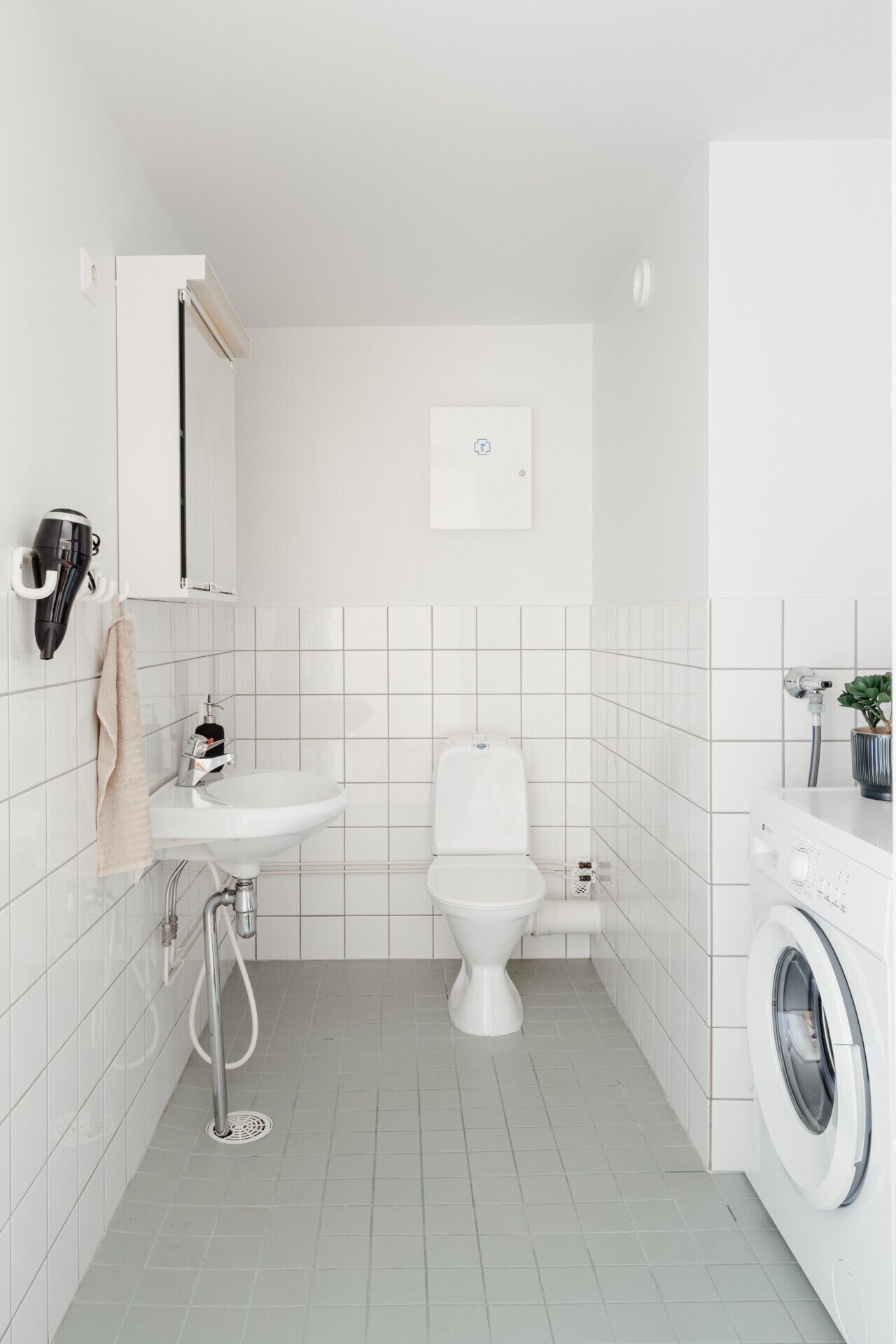 A compact, modern bathroom with a white sink, toilet, and washing machine.