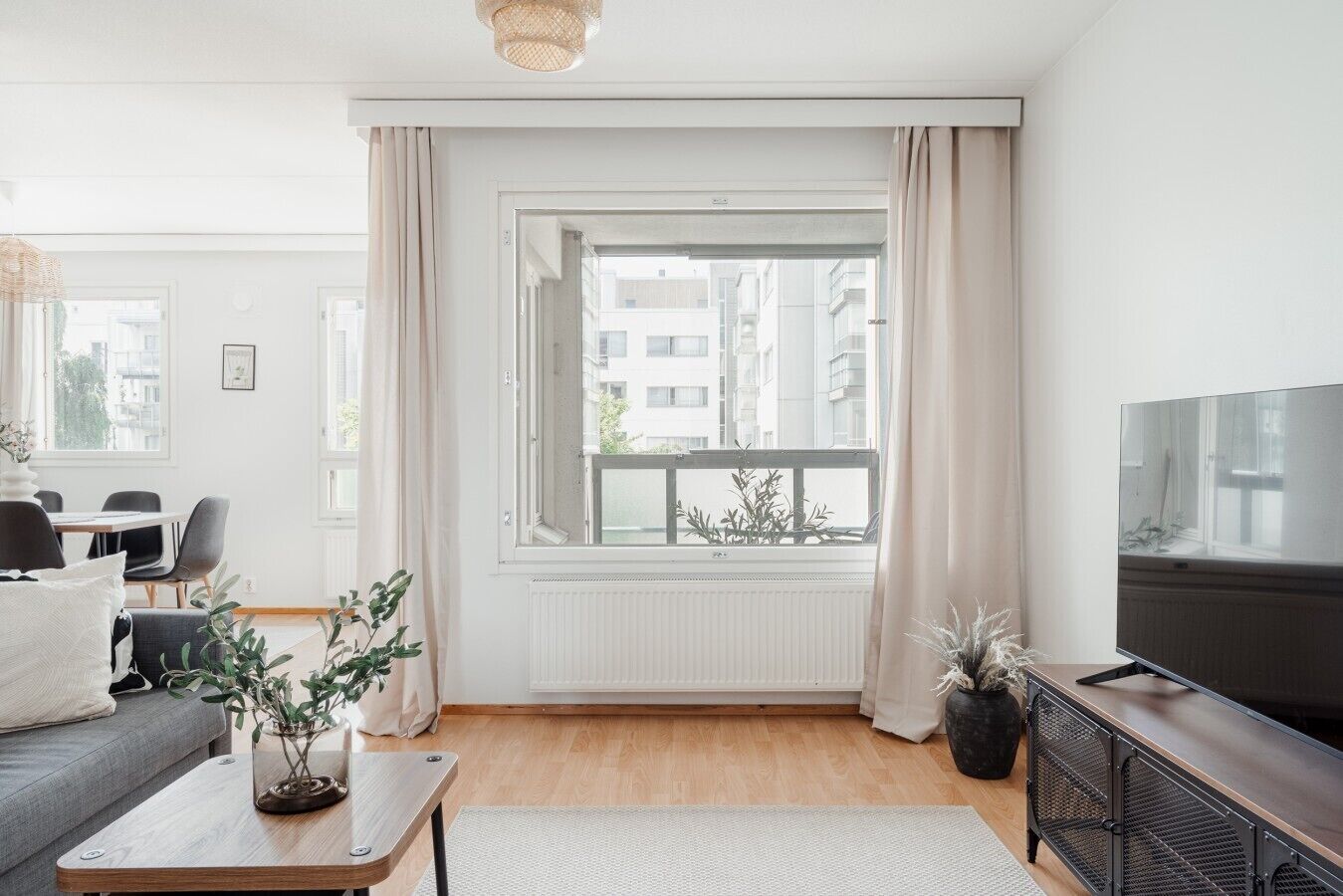 A modern living room with a large window, a flat-screen TV, and a dining area with chairs and a table.