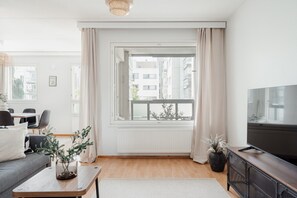 Een moderne woonkamer met een groot raam, een flatscreentelevisie en een eethoek met stoelen en een tafel.
