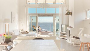 A spacious room with a large bed, a seating area with a view of the sea, and a television on a stand. - Villa with Panoramic Water Views (Makkum)