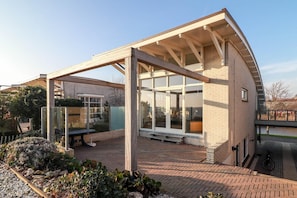 A modern house with a covered patio, a glass door, and a brick exterior. - Villa with Panoramic Water Views (Makkum)