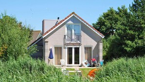 Ein zweistöckiges Haus mit Balkon, einer Veranda mit Stühlen und einem Rasen.