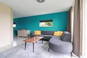A modern living room with a grey sofa, a wooden coffee table, and a teal accent wall. - Comfortable 4-Person Bungalow with Jetty (Makkum)