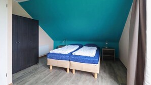 Ein Schlafzimmer mit schrägem Dach, einem Bett mit blauer Matratze, einem Nachttisch und einem Kleiderschrank.