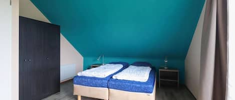 Ein Schlafzimmer mit schrägem Dach, einem Bett mit blauer Matratze, einem Nachttisch und einem Kleiderschrank.