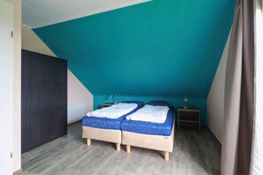 A bedroom with a sloped ceiling, a bed with a blue mattress, a bedside table, and a wardrobe. - Comfortable 4-Person Bungalow with Jetty (Makkum)