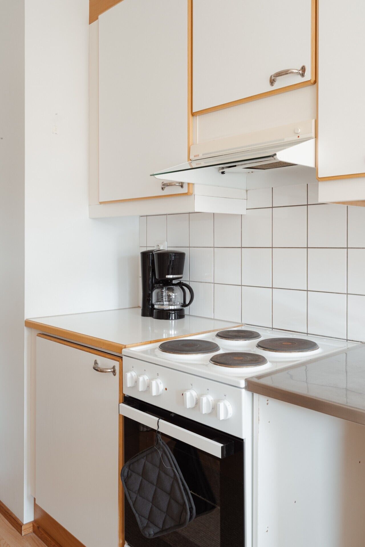 Ett kompakt kök med vita skåp, en spis och en kaffebryggare.