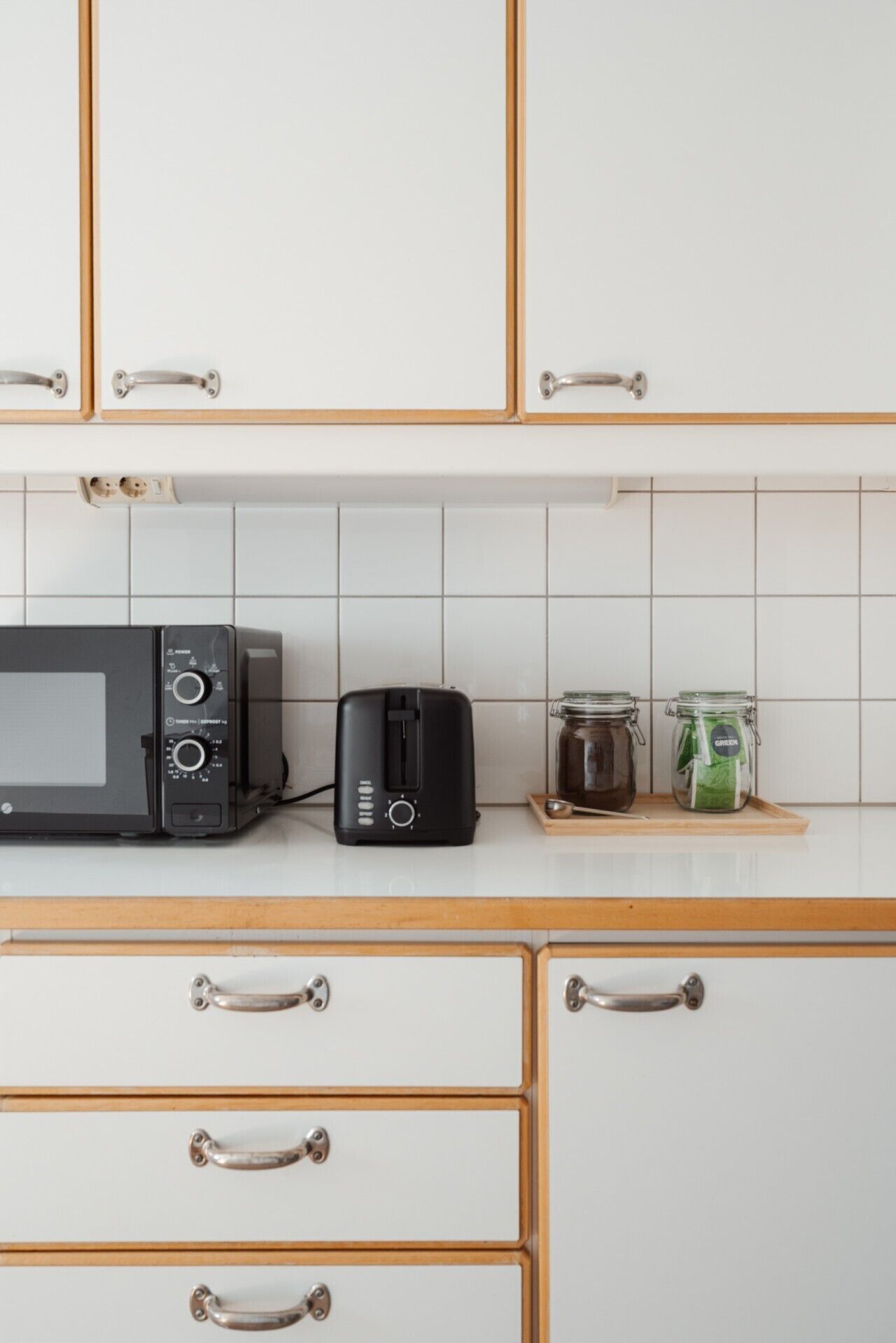 A kitchen with white cabinets, a microwave, a toaster, and two jars on the counter.
