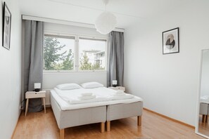Un dormitorio moderno con una cama grande, dos mesitas de noche, una ventana con cortinas y una lámpara colgante.