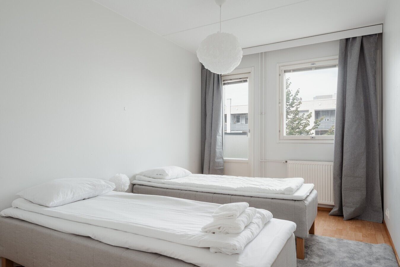 Un dormitorio con dos camas, una ventana con cortinas y una lámpara colgante.