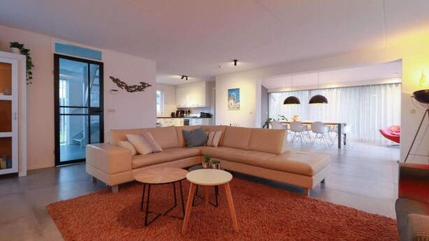 Uma sala de estar moderna com um sofá em L, duas mesinhas redondas e um tapete vermelho.