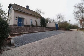 Ein Gebäude mit einem Strohdach, einer blauen Tür und einer gepflasterten Auffahrt, die zu einem Kiesplatz führt.