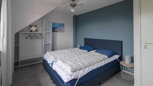 Quarto com cama, ventilador de teto, prateleira na parede com um salva-vidas e um quadro.