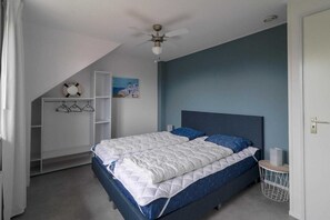 Ein Schlafzimmer mit einem Bett, einem Deckenventilator, einem an der Wand befestigten Regal mit einem Rettungsring und einem Gemälde.