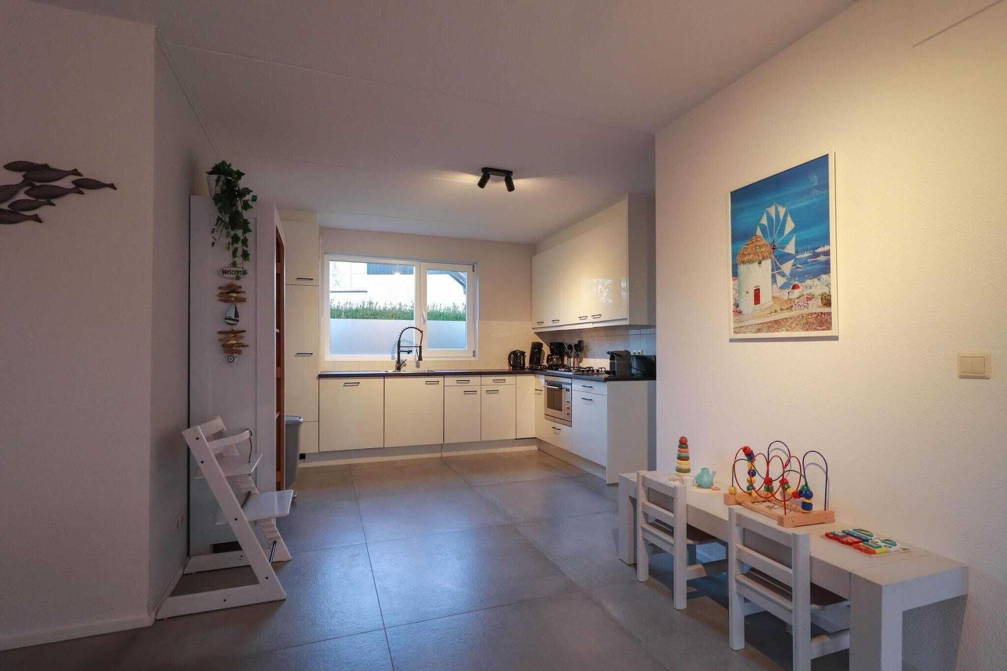 A modern kitchen with white cabinets, a dining area with a table and chairs, and a view of the outdoors through a window.