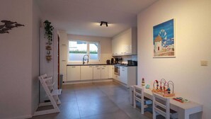 Uma cozinha moderna com armários brancos, um espaço de jantar com mesa e cadeiras, e vista para o exterior através de uma janela.