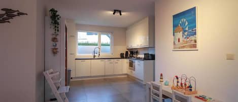 A modern kitchen with white cabinets, a dining area with a table and chairs, and a view of the outdoors through a window.