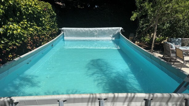 En pool med en överbyggd del, omgiven av träd och utomhusmöbler.