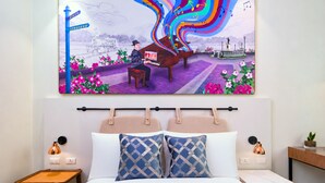 Une chambre d’hôtel comprenant un lit, deux tables de chevet, une tête de lit et un grand tableau mural représentant un homme jouant du piano en plein air.