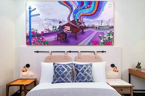 A hotel room with a bed, two nightstands, a headboard, and a large wall painting of a man playing a piano outdoors. - MCollection - Modern City Stay in Iloilo Business Park (Iloilo)