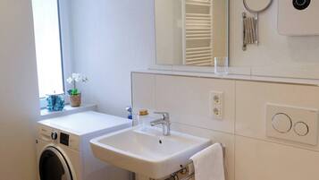 Ein kleines Badezimmer mit Waschmaschine, Waschbecken, Toilette und Spiegel.