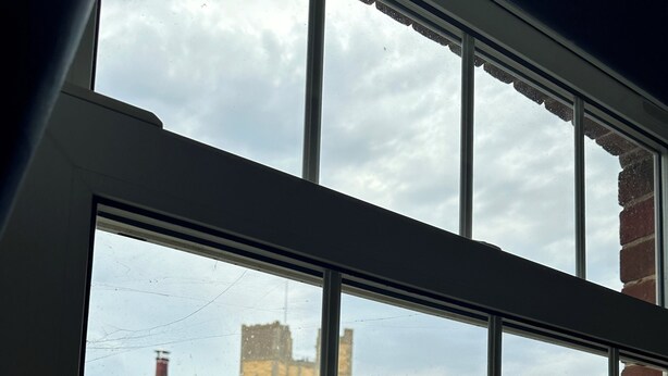 Ein Fenster mit Blick auf ein Backsteingebäude und Grünflächen.