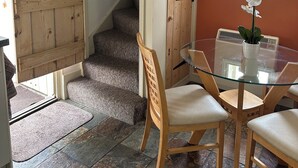 Ein Essbereich mit einem Glastisch, Holzstühlen, einer Topfpflanze und einer Treppe zu einer weiteren Ebene.