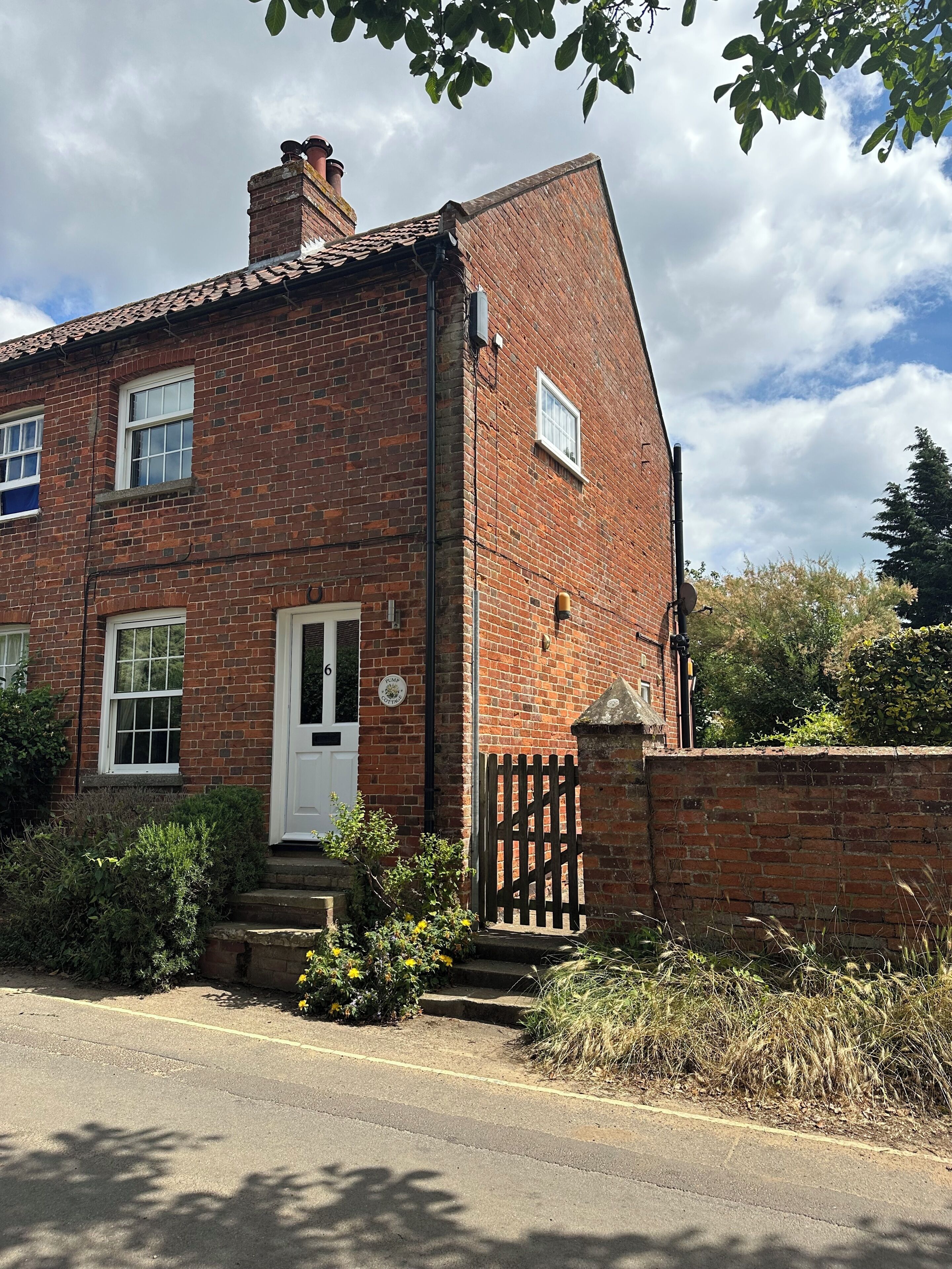A two-story brick house with a white door, a small front garden, and a brick wall.