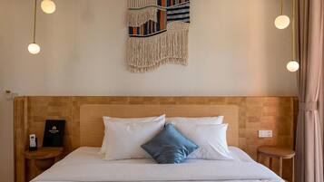 Hotelkamer met een houten hoofdeinde, een bed met witte en blauwe kussens, een wanddecoratie en een nachtkastje met een telefoon.