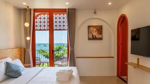 A hotel room with a bed, a television, a painting, and a view of the sea through a large window. - The Dome Hòn Thơm Hotel (Phu Quoc)