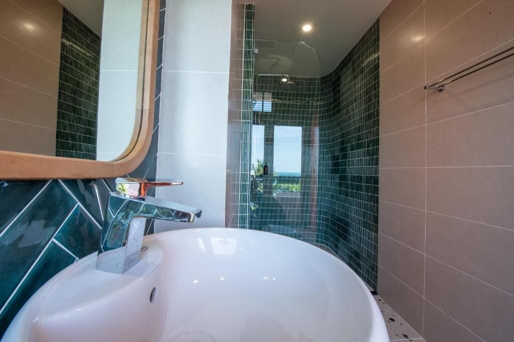 A modern bathroom with a white sink, a mirror, and a shower area.
