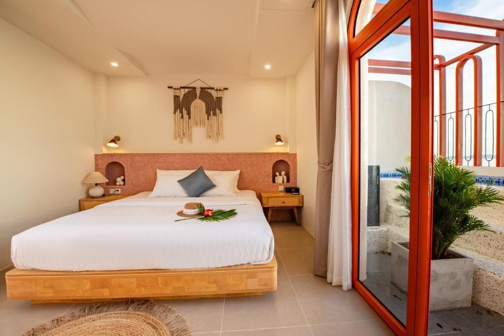 A bedroom with a large bed, bedside tables, a wall-mounted light fixture, and a view through a glass door to an outdoor area.