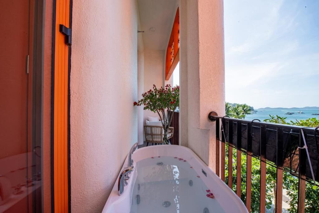 A balcony with a hot tub, a view of the sea, and a small seating area with a plant.