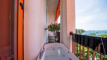 A balcony with a hot tub, a view of the sea, and a small seating area with a plant.
