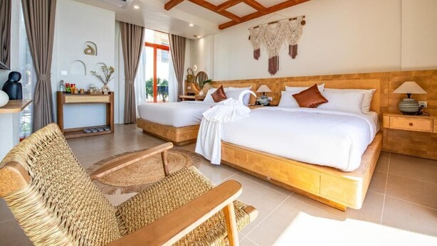 A hotel room with two beds, a sitting area with a woven chair, and a wooden ceiling. - The Dome Hòn Thơm Hotel (Phu Quoc)