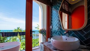 A bathroom with a large white sink and a pink bathtub, a red-framed mirror, and a view of the ocean. - The Dome Hòn Thơm Hotel (Phu Quoc)
