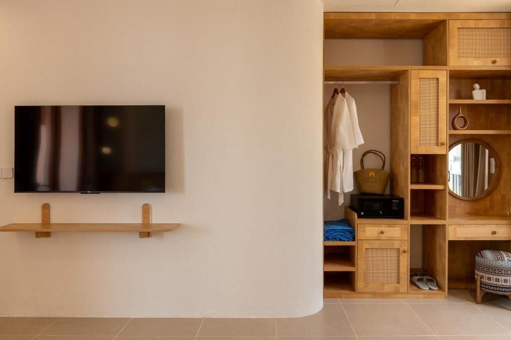 Una habitación moderna con una televisión de pantalla plana montada en la pared, un banco de madera, un armario con espejo y un taburete pequeño.