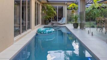 A swimming pool with a clear blue water surface, surrounded by a covered patio area with potted plants and outdoor furniture.
