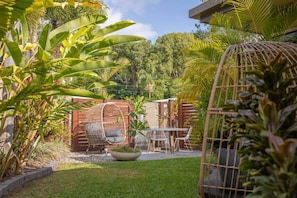 A patio with a table and chairs, surrounded by lush greenery and a wooden fence.