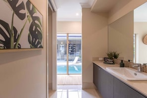 Une salle de bain moderne avec un grand miroir, un lavabo et une vue sur l’espace piscine, visible à travers des portes vitrées.