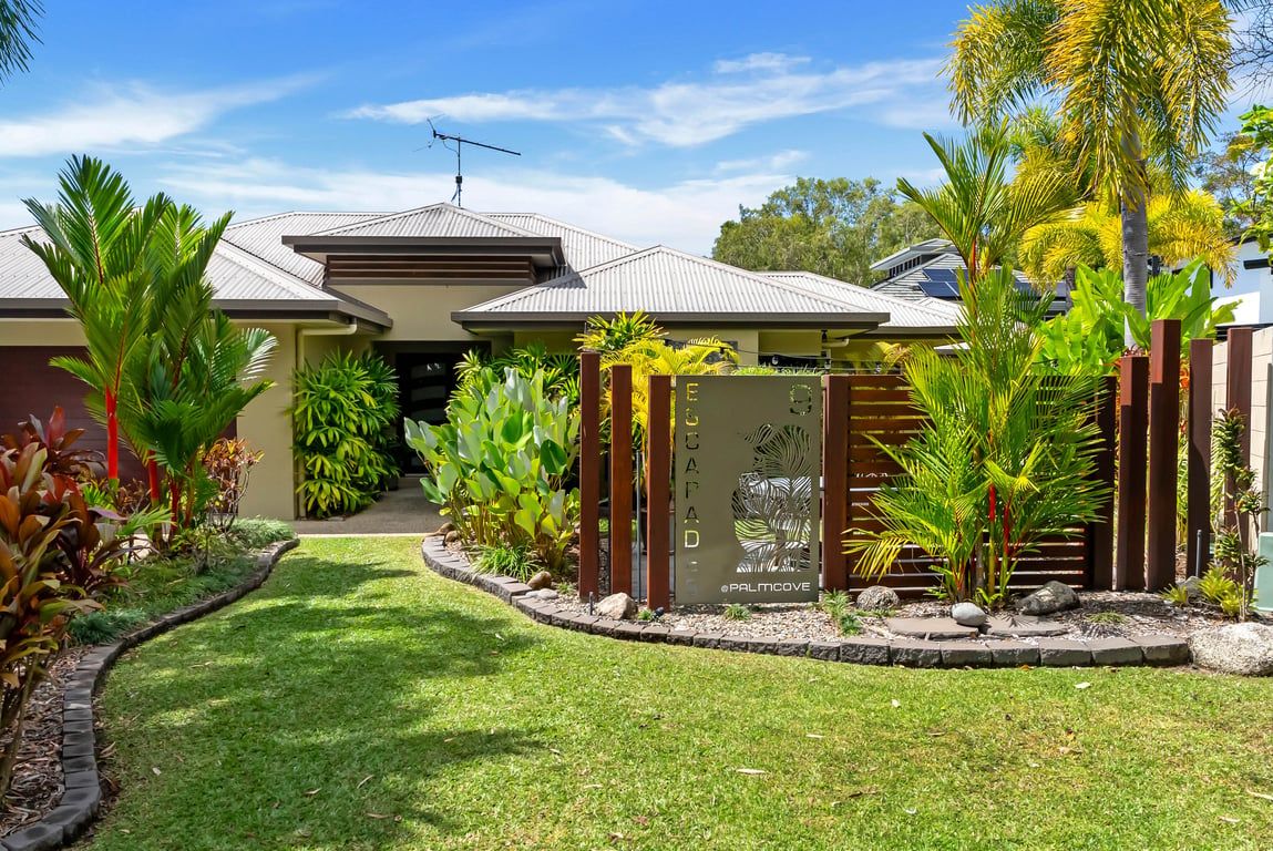 A residential property with a well-maintained lawn, a gated entrance, and a variety of tropical plants.
