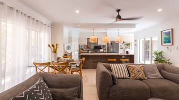 A modern living room with a sofa, a dining table with chairs, and a kitchen area in the background.