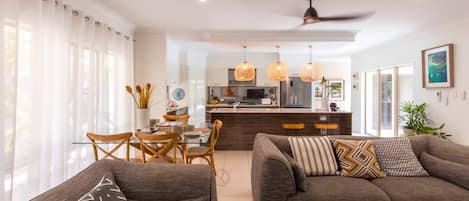 A modern living room with a sofa, a dining table with chairs, and a kitchen area in the background.