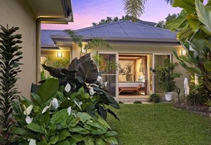 A modern house with a well-maintained garden, a visible interior with a sofa and a dining area, and a clear sky at dusk.