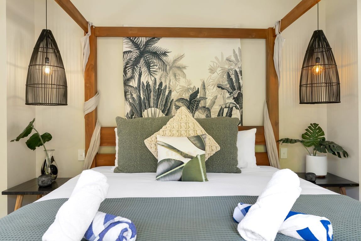A hotel room with a bed, two bedside tables, a wall tapestry, and a potted plant.