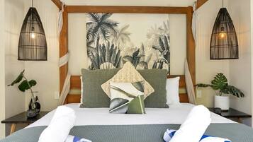 A hotel room with a bed, two bedside tables, a wall tapestry, and a potted plant.